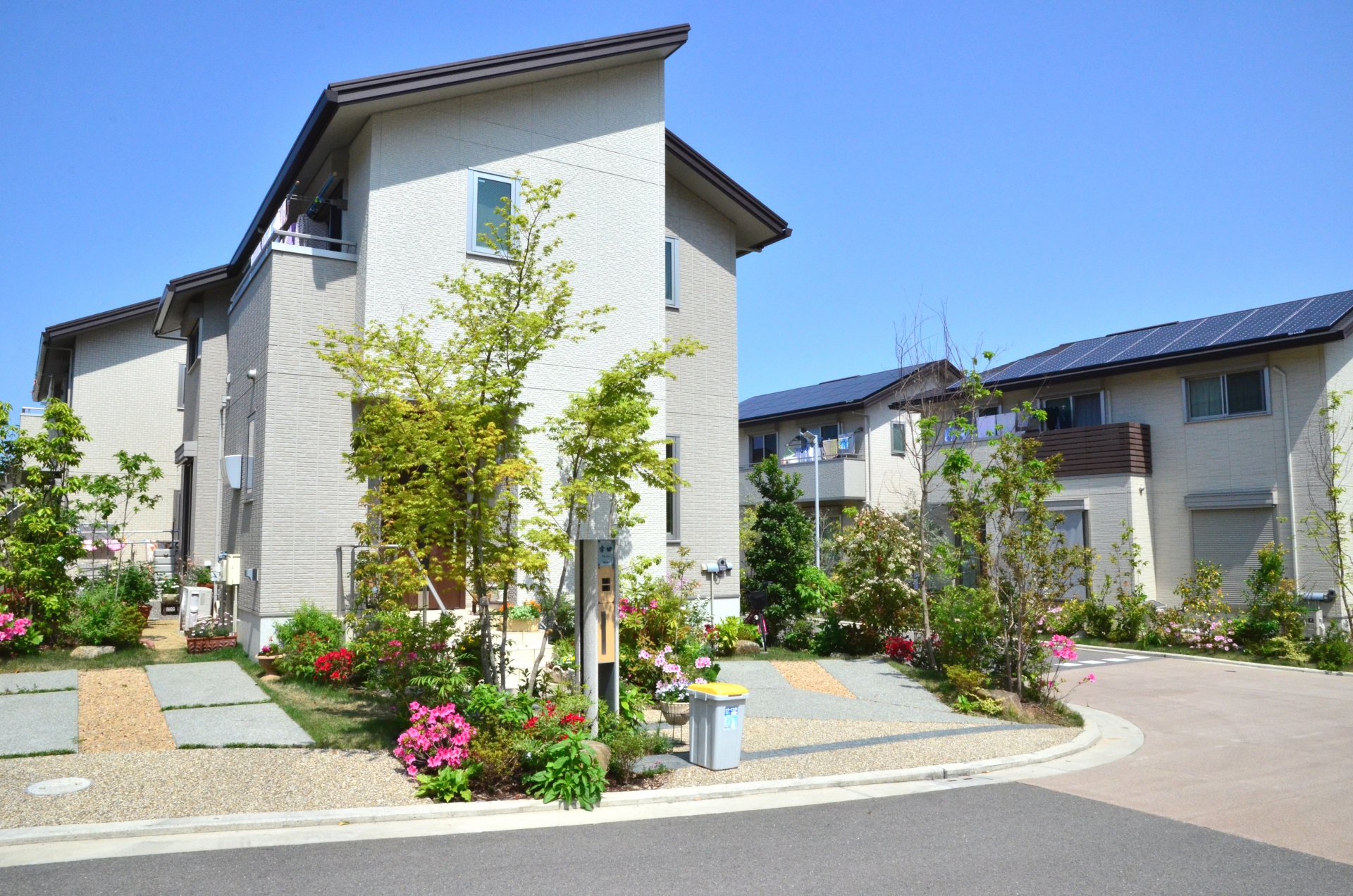 青空の下、庭木や花が彩る住宅街の一角